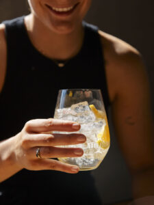 Woman in a black singlet holding a glass filled with a clear liquid and ice cubes.