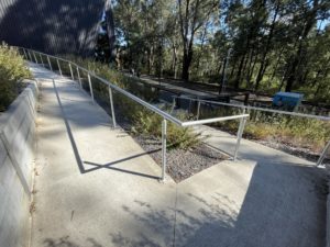 Paved walkway with white picket fence to a train platform.