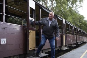 A man is disembarking the open side carriage. He is stepping down onto the platform and is holding on to the carriage doorway for balance.