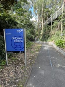 Pathway From Belgrave Metro Train Station To Puffing Billy Railway. The path has a bitumen surface and is quite narrow. It shows a blue line directing visitors to Puffing Billy from Metro.