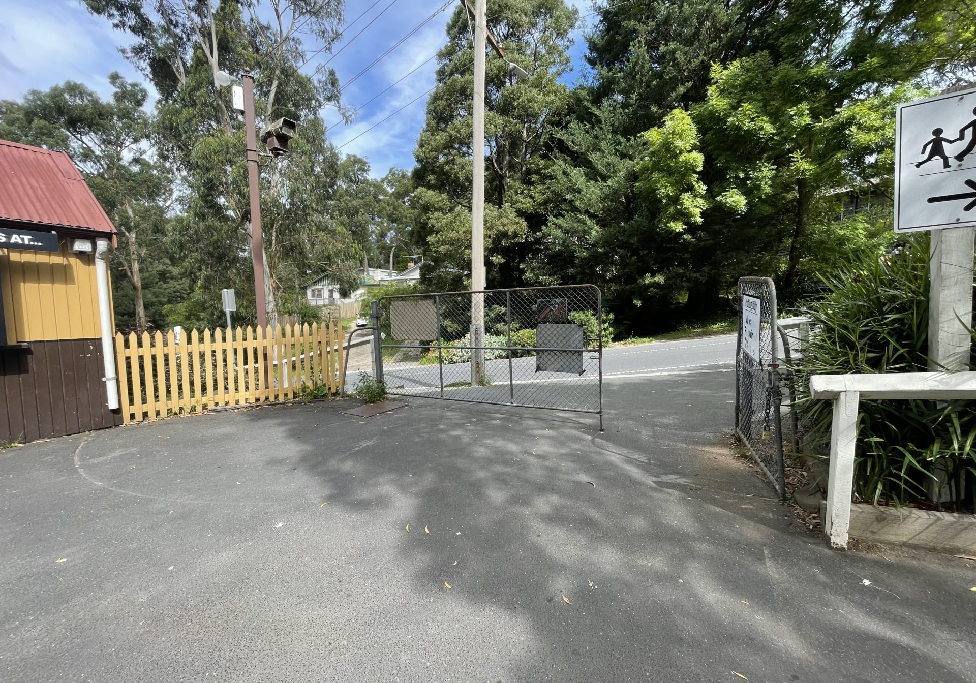 Belgrave Station's drop off zone at Gate 4 is on one level with a bitumen surface. A steel gate is open, and a Puffing Billy building in heritage colours can be seen to one side.