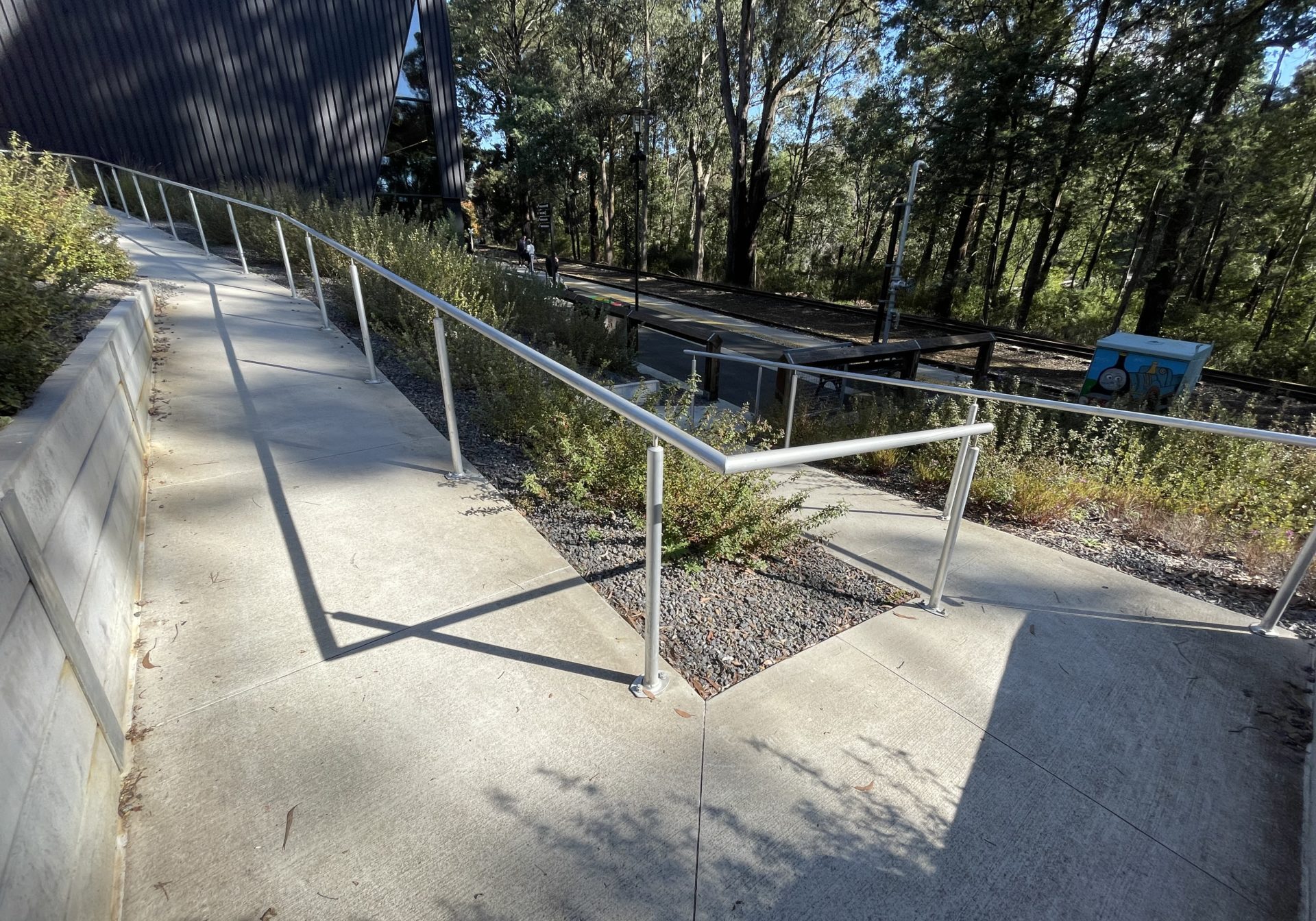 Paved walkway with white picket fence to a train platform.
