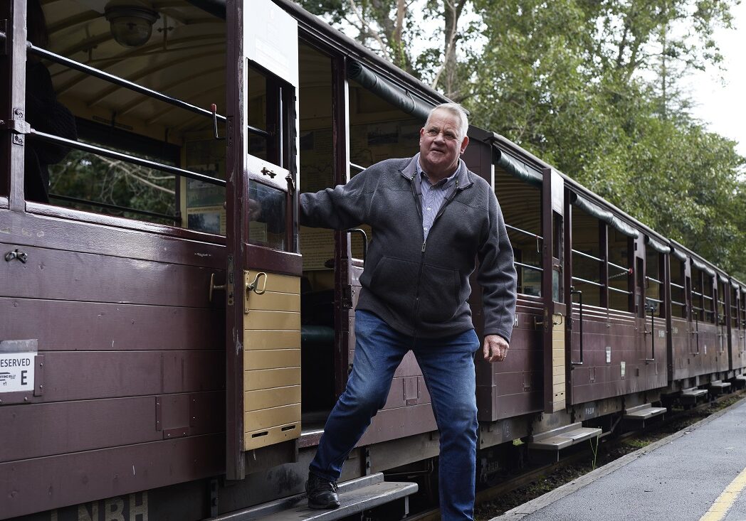 A man is disembarking the open side carriage. He is stepping down onto the platform and is holding on to the carriage doorway for balance.