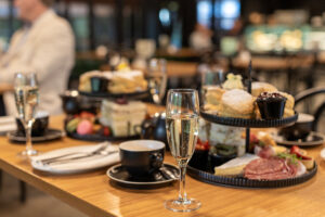 High tea served on tiered stands, with coffee and glasses of sparkling wine next to them.
